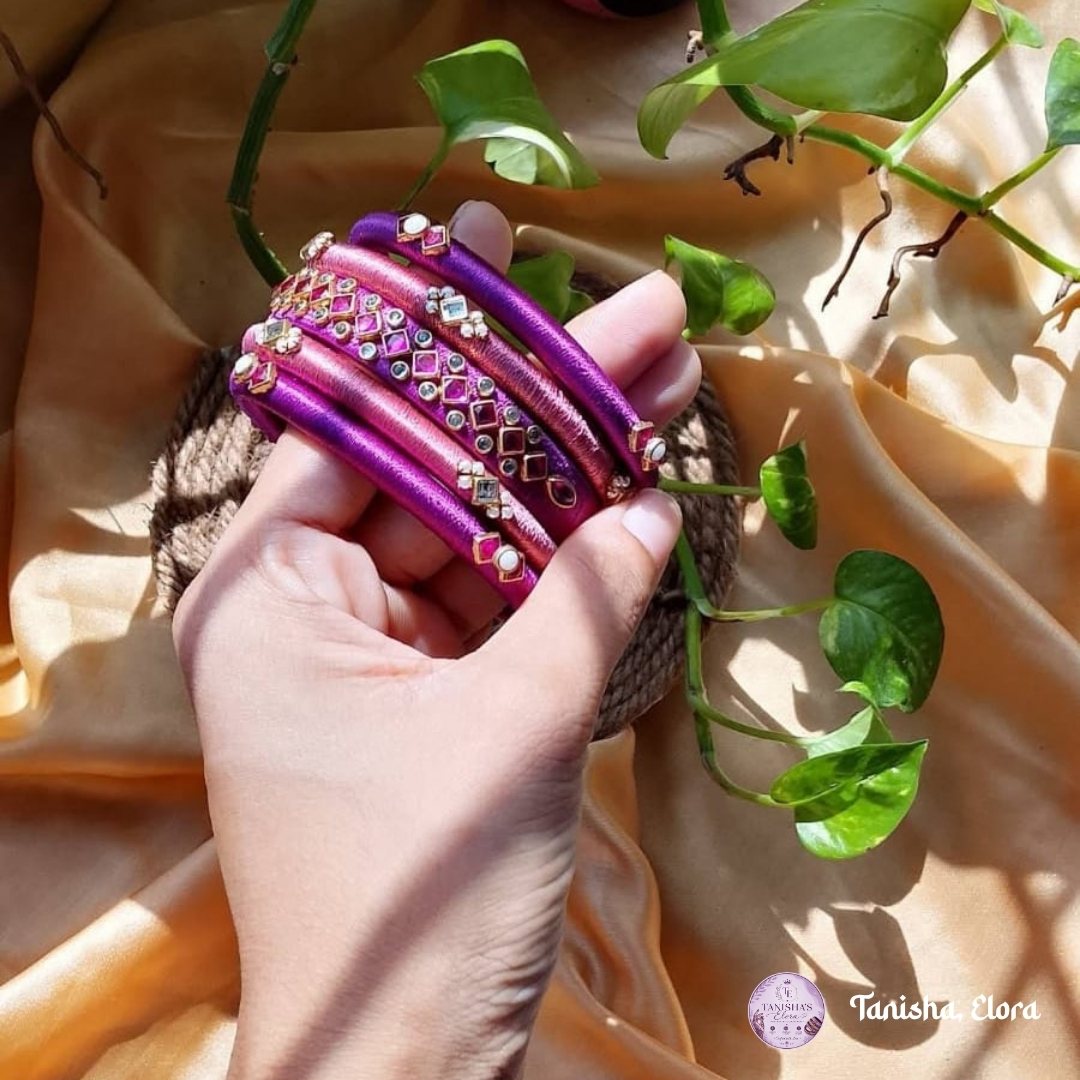 Hand holding a stack of magenta and gold Churi bangles